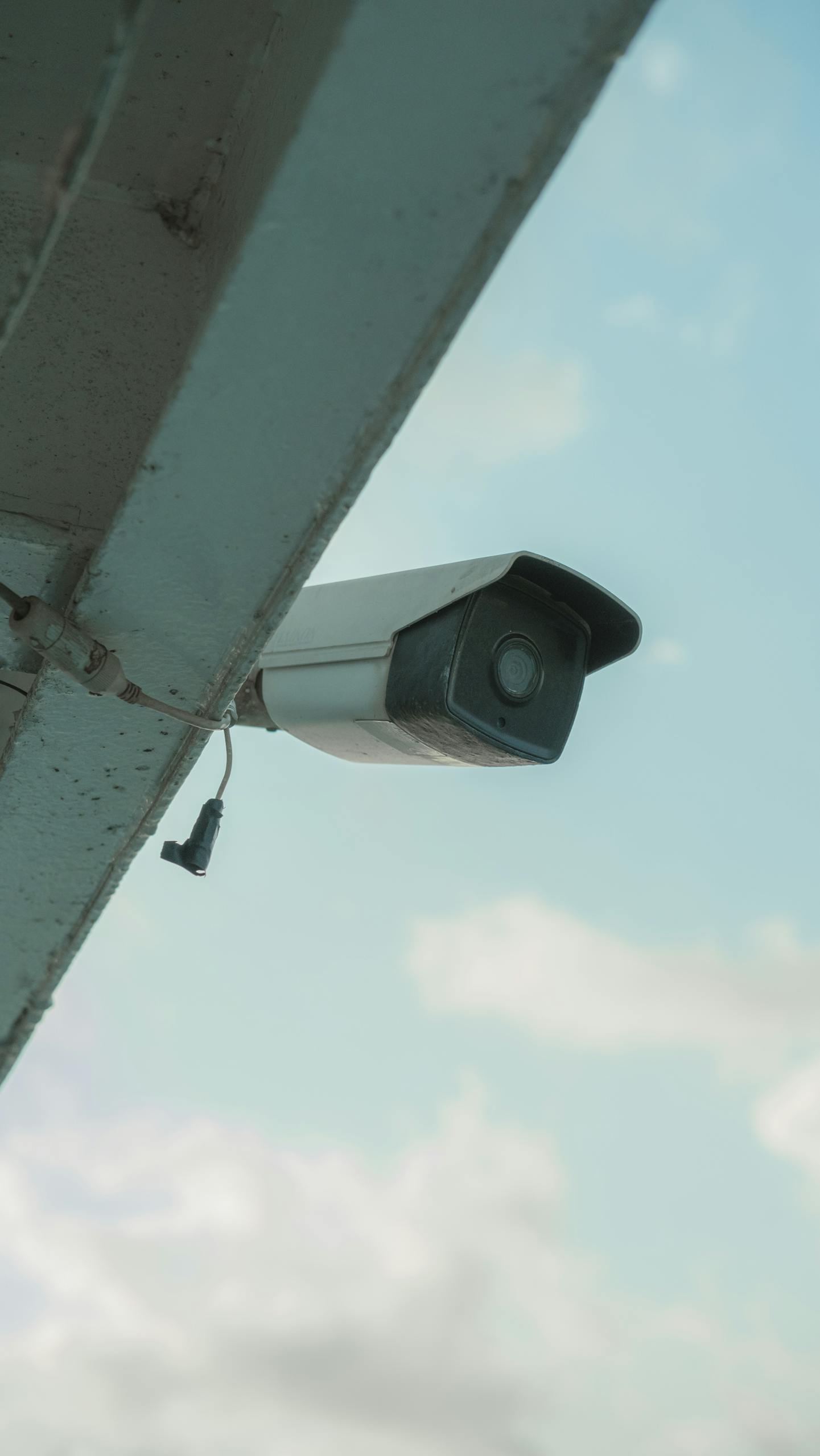 A security camera mounted on a building eaves under a clear blue sky.
